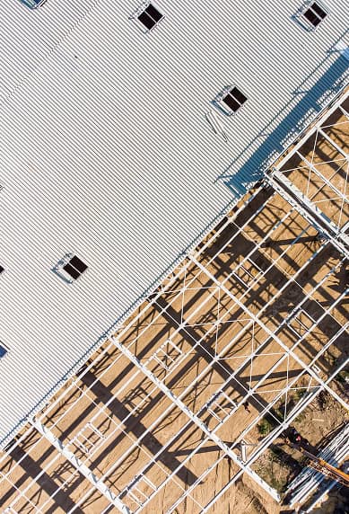 Aerial view of a building under construction in South Carolina, featuring a metal roof with skylights and exposed steel framework casting shadows—expertly crafted by Clover Roofing.