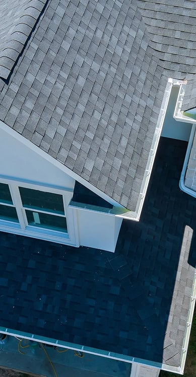 Aerial view of a house roof with gray asphalt shingles and white trim, showing part of a sloped roof and windows—expertly crafted by Clover Roofing, serving South Carolina homes with quality and care.