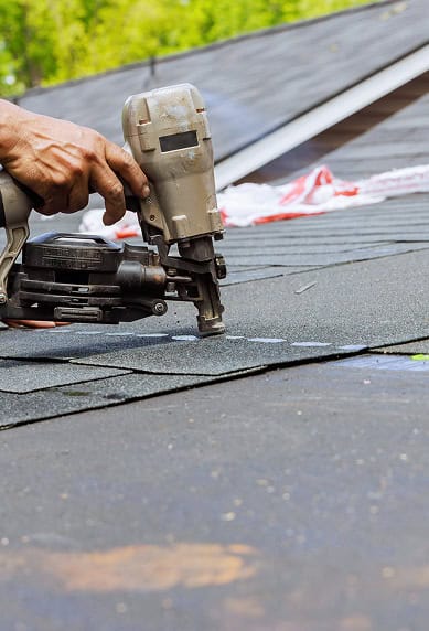 A person uses a pneumatic nail gun to install asphalt shingles on a roof for Clover Roofing in South Carolina.
