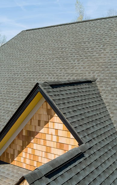 A close-up view of a house roof with dark gray asphalt shingles and a dormer featuring new, light-colored wooden siding, expertly installed by Clover Roofing in South Carolina.