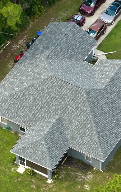 Aerial view of a gray-roofed house by Clover Roofing, with several cars parked in the driveway and green grass surrounding the South Carolina property.