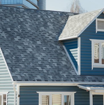 Close-up view of a modern house with blue siding and a roof covered in gray asphalt shingles, expertly installed by Clover Roofing in South Carolina.