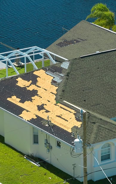 A house in South Carolina with a roof missing many shingles, exposing the wooden underlayment—likely due to storm damage—could benefit from expert repairs by Clover Roofing.